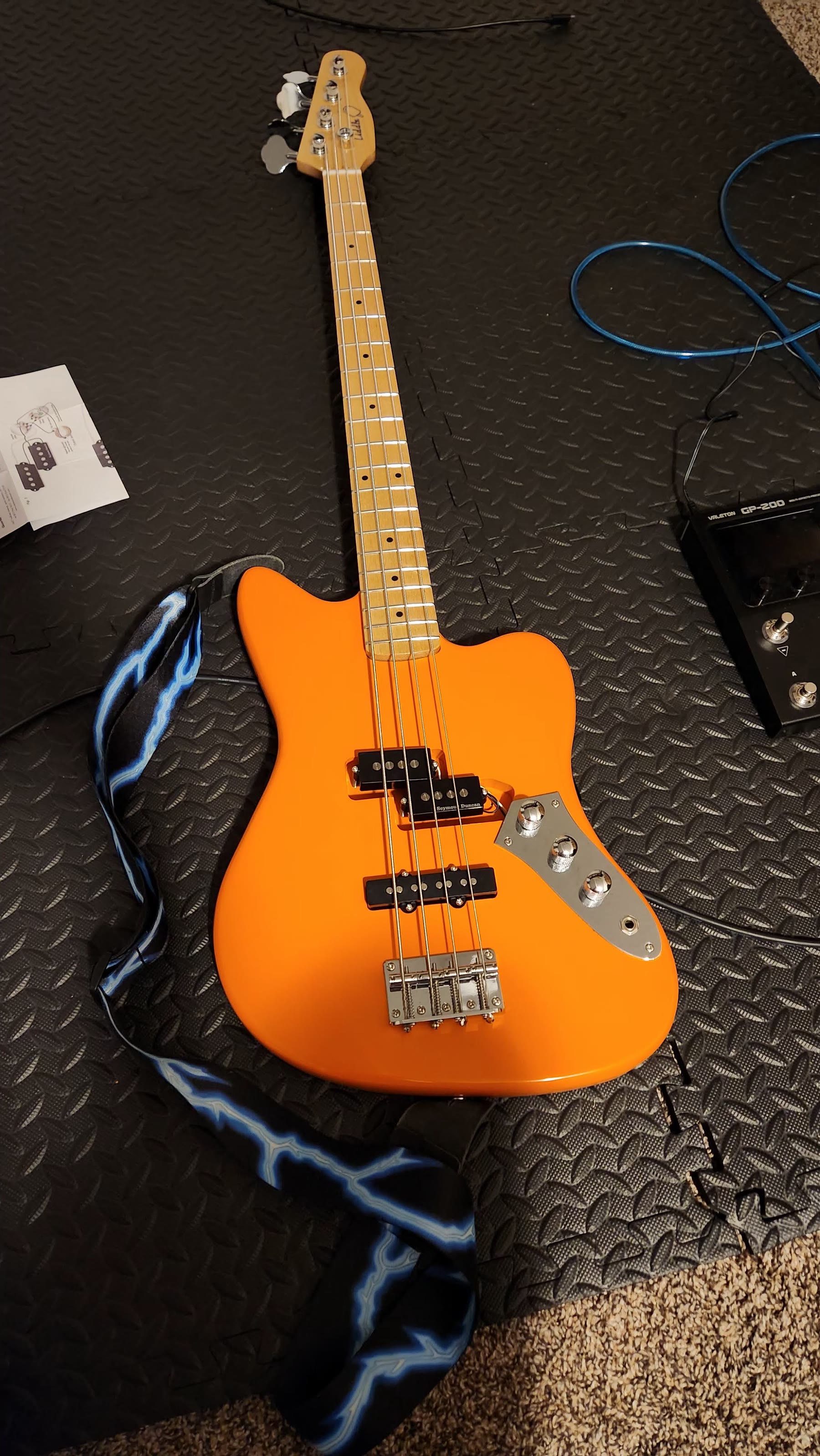 Completed orange electric bass guitar standing on a wooden floor